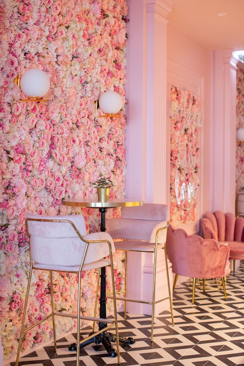 Interior da Nês com parede floral, poltronas rosa e mesas redondas